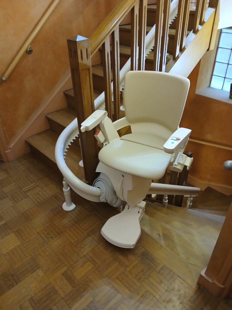 Départ du rail et monte-escalier courbe en position basse au pied d'un escalier en bois